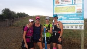a team of four women standing in front of the trail map at the start of a trail 