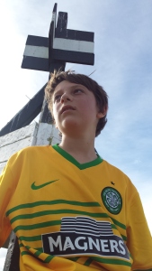 teenage boy wearing a yellow and green football shirt sitting under a Trig point in New Zealand
